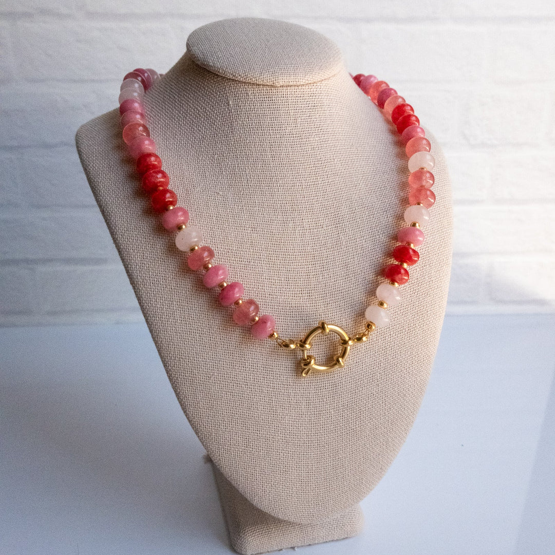 Necklace with pink beads and a gold clasp on a beige bust against a white background