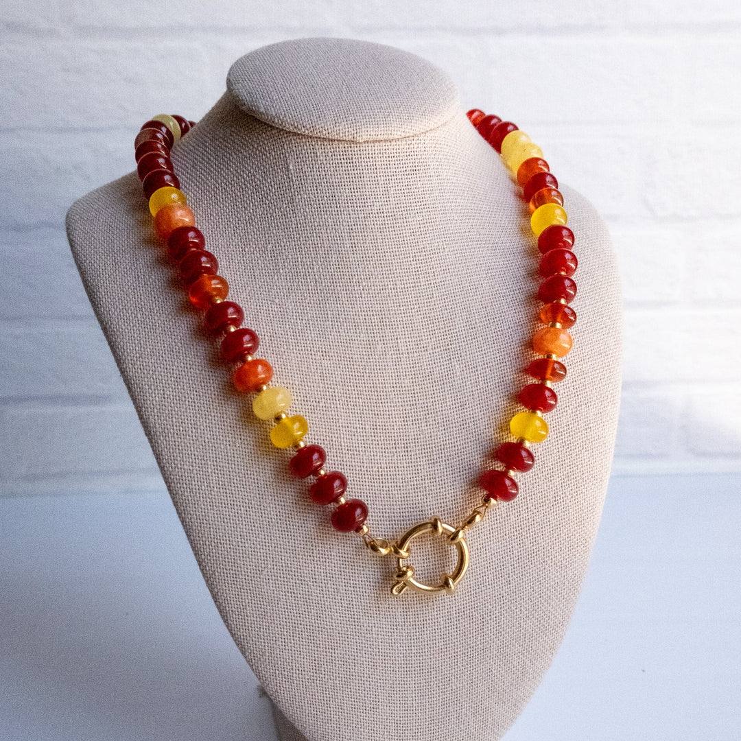 Necklace with red, yellow, and brown beads on a beige bust against a white background