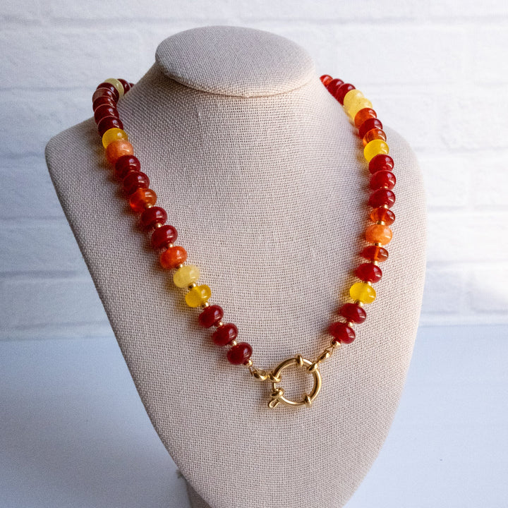 Necklace with red, yellow, and brown beads on a beige bust against a white background