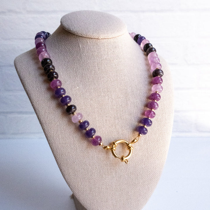 Necklace with purple and black beads on a beige bust against a white background