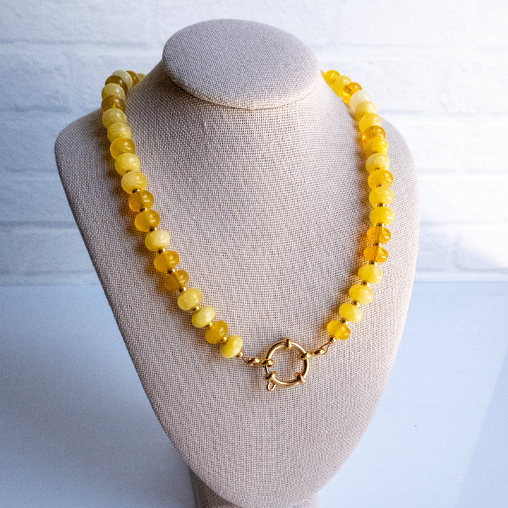 Yellow beaded necklace on a beige bust against a white background
