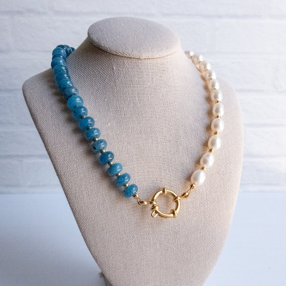 Necklace with blue beads, pearls, and a gold clasp on a beige bust against a white background