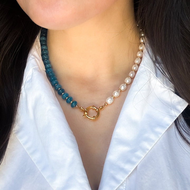 Pearl necklace with blue beads and gold clasp worn by a person in a white shirt.