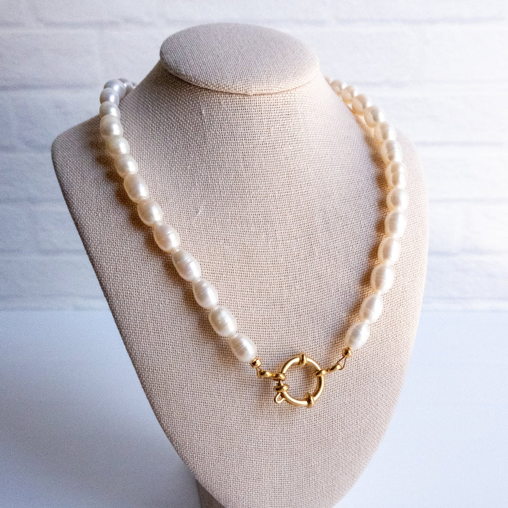 Pearl necklace with a gold clasp on a beige bust against a white background
