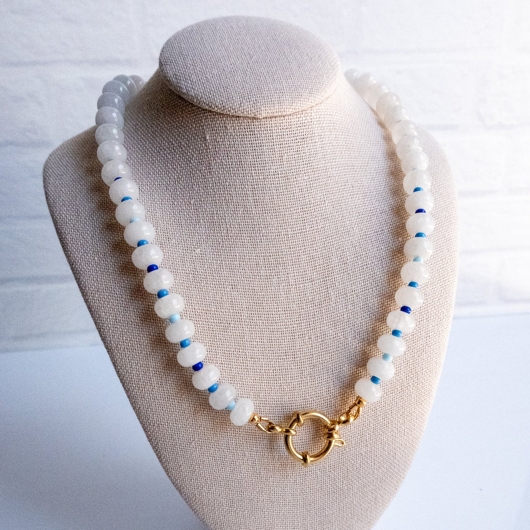 Necklace with white beads and a gold clasp on a beige bust against a white background