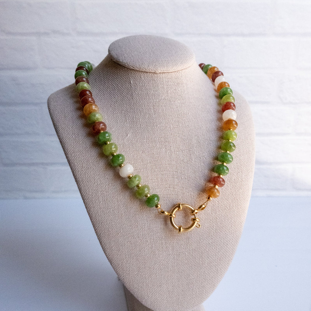 Necklace with multicolored beads and a gold clasp on a beige bust against a white background