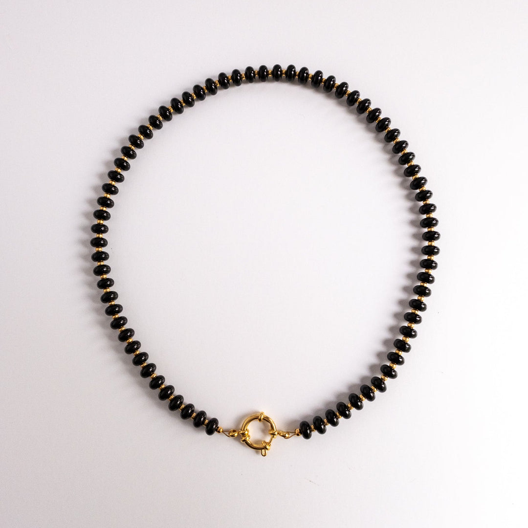 Black beaded necklace with a gold clasp on a light gray background