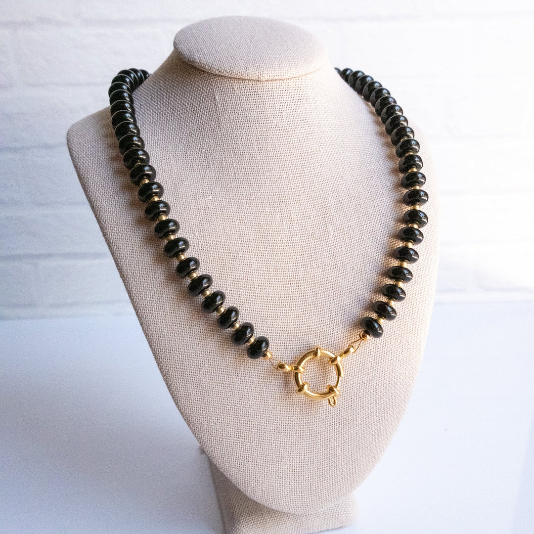 Necklace with black beads and gold clasp on a beige bust against a white background