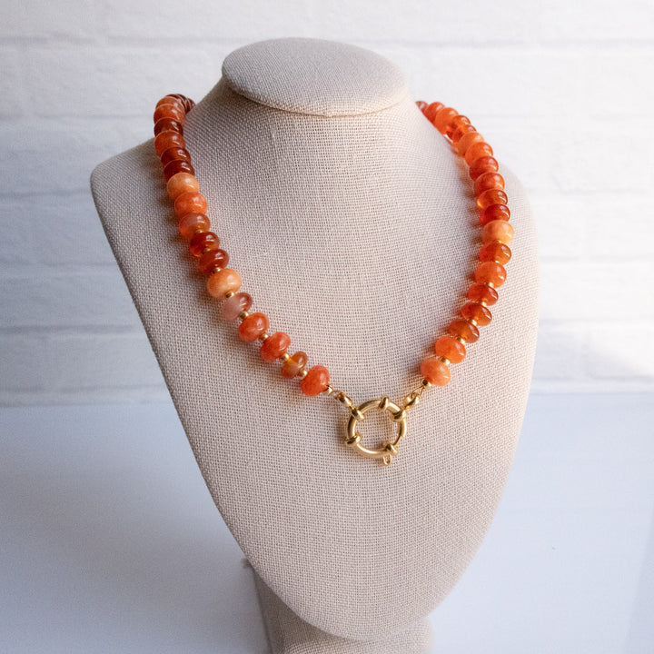 Necklace with orange beads on a beige mannequin bust against a white background
