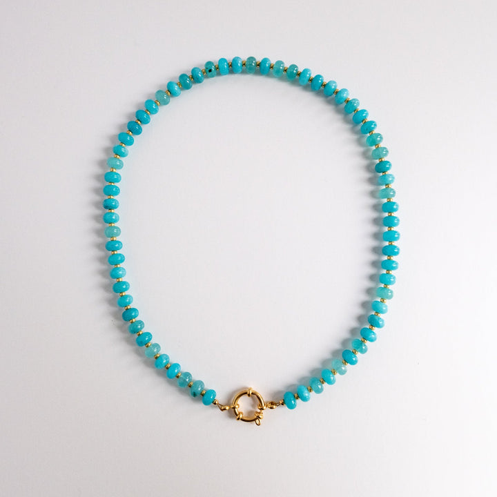 Turquoise beaded necklace with a gold clasp on a light gray background