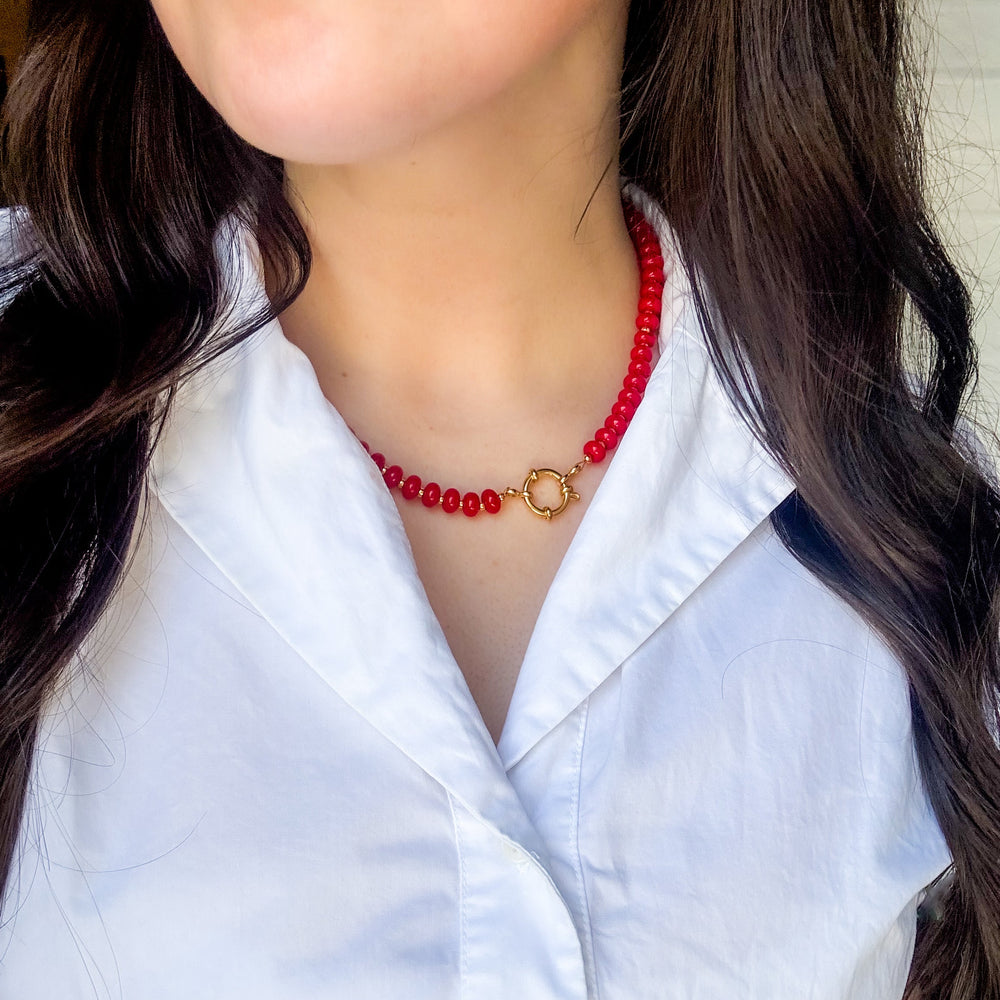 Person wearing a red beaded necklace with a white shirt