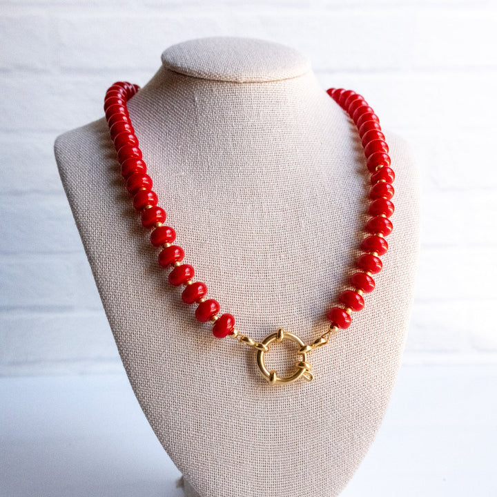 Red beaded necklace with a gold clasp on a beige mannequin bust against a white background