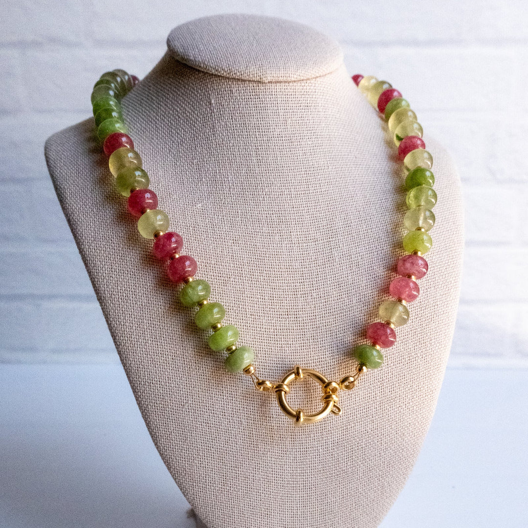 Necklace with green and pink beads on a beige bust against a white background